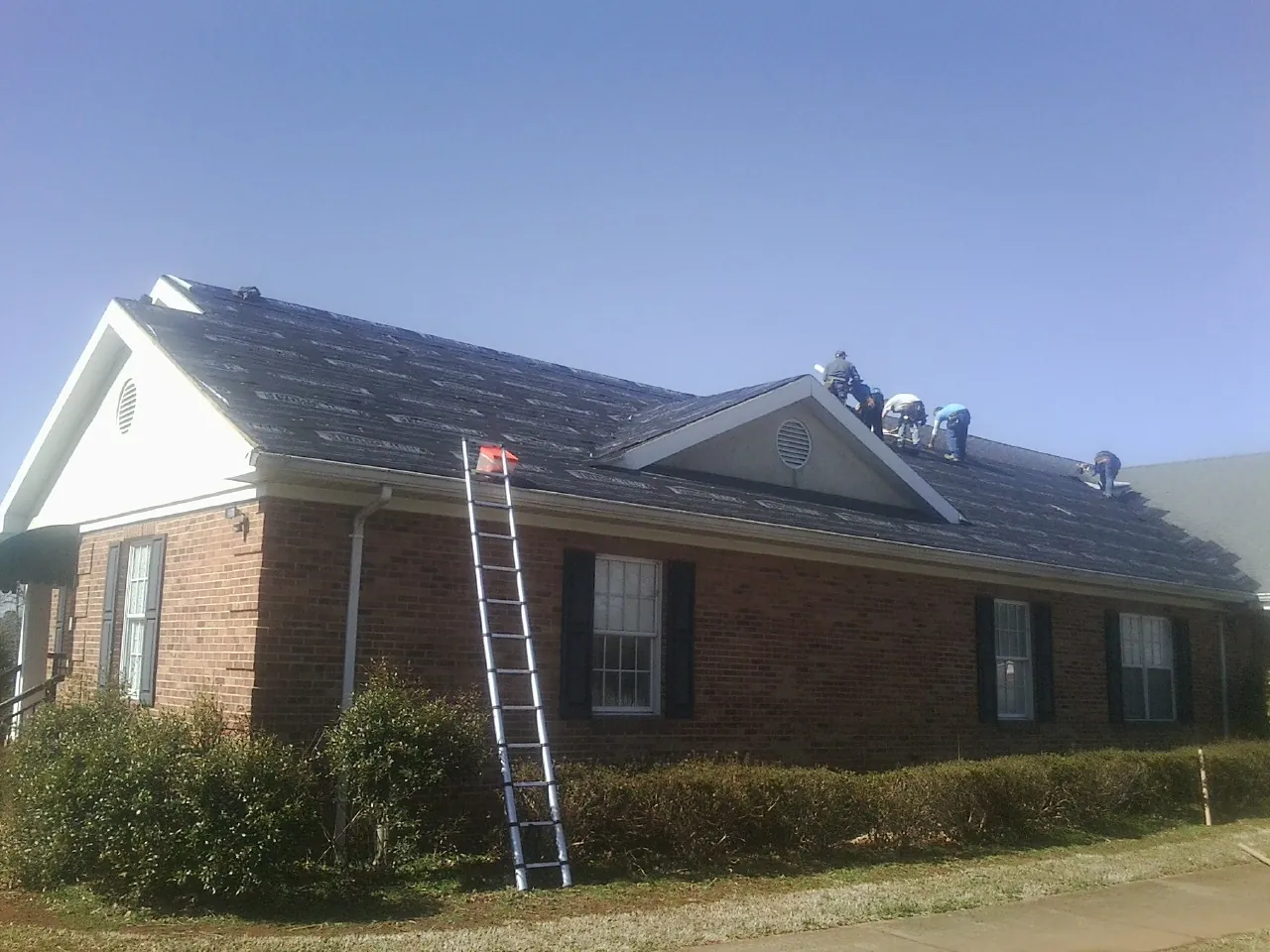 Crew tearing shingles off a brick ranch roof with a ladder set — Emergency Roof Repair work by our crew in West Newbury