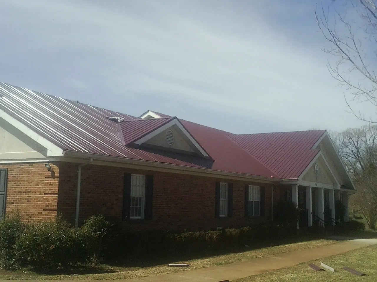 Red metal roof with gabled entries on a long brick building, from a Hail Damage Roof Repair job in West Newbury