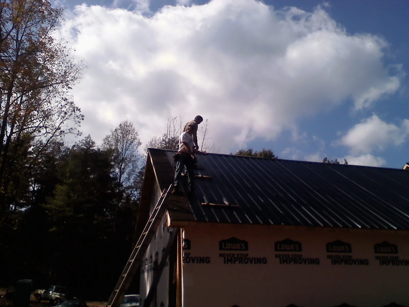 Roofer fastening dark metal panels high against a cloudy sky, from a Roof Inspection job in West Newbury