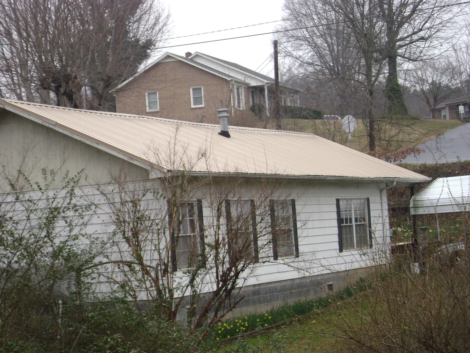 Tan metal roof on a white sided house set into a hillside — Commercial Roofing by Roofing Brothers in West Newbury